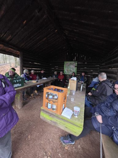 Gruppe von Personen sitzt in einer Hütte um einen Tisch, darunter Getränke und Notizen.