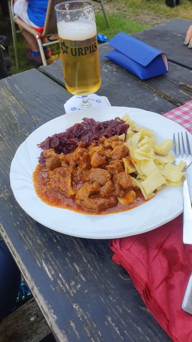 Ein Teller mit Fleischgericht, Rotkohl, Nudeln und einem Glas Bier.