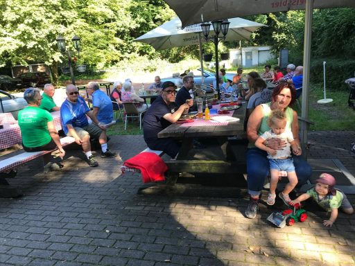 Familienpicknick im Freien mit mehreren Personen an Tischen unter Sonnenschirmen.