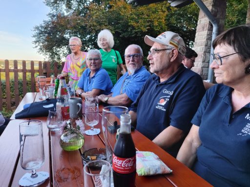 Gruppe von sechs Personen sitzt an einem Tisch im Freien, umgeben von Pflanzen.