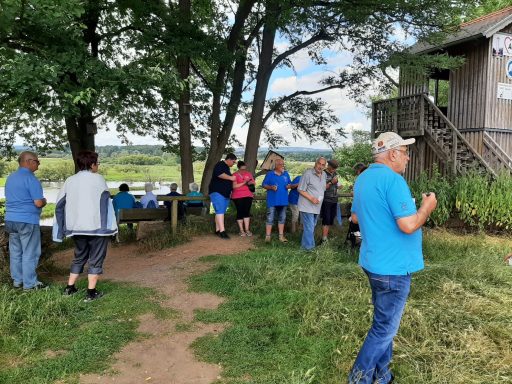Gruppe von Menschen bei einem Treffen im Freien, umgeben von Natur und Bäumen.