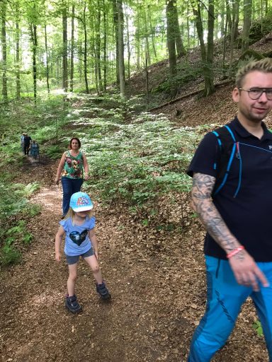 Familie wandert auf einem schmalen Weg durch einen bewaldeten Bereich.