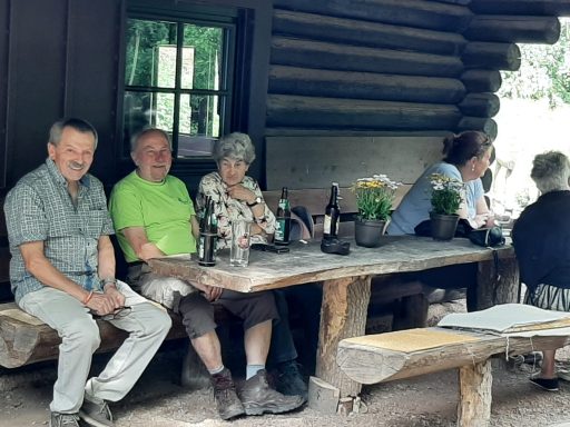Drei Personen sitzen an einem Holztisch unter einem Dach, ruhig und entspannt.