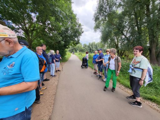 Gruppe von Menschen am Wegesrand, umgeben von Bäumen, einige halten Smartphones.
