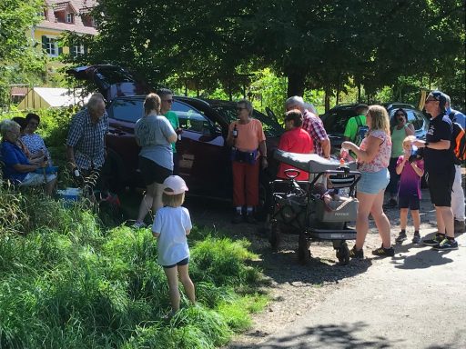 Eine Gruppe von Menschen, darunter Kinder, steht bei einem Parkplatz im Freien.