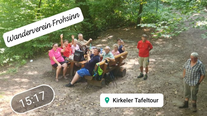 Gruppe von Wanderern im Wald, einige sitzen auf einer Bank, andere stehen daneben.