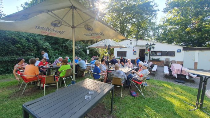 Gruppentreffen im Freien, Tische und Stühle unter Sonnenschirmen, entspannte Atmosphäre.