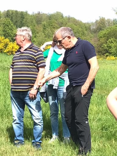 Drei Personen stehen auf einer Wiese, eine hält die Hand eines anderen.