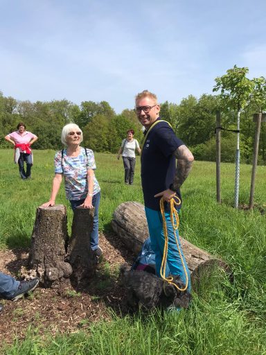 Gruppe von Personen, die im Freien an Baumstümpfen stehen, umgeben von Grün.