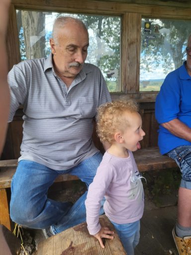 Ein älterer Mann sitzt neben einem lächelnden kleinen Mädchen in einer Holzstruktur.