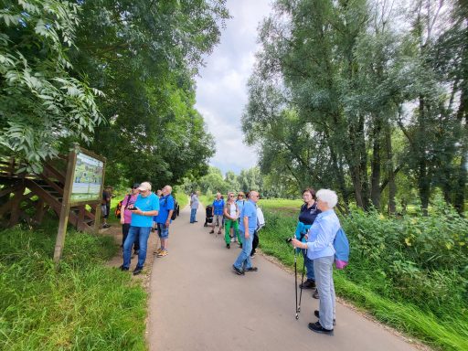 Gruppe von Wanderern auf einem Weg zwischen Bäumen und Wiesen, einige stehen und reden.