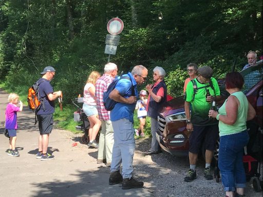Gruppen von Wanderern am Wegesrand, einige mit Rucksäcken, andere in Gesprächen.