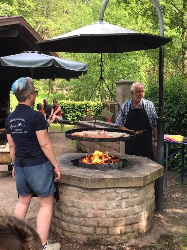 Eine Person grillt bei einem Außenbereich, während eine andere zuschaut.