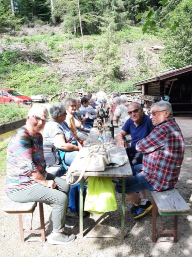 Gruppe von Menschen sitzt an einem Tisch im Freien, umgeben von Natur.