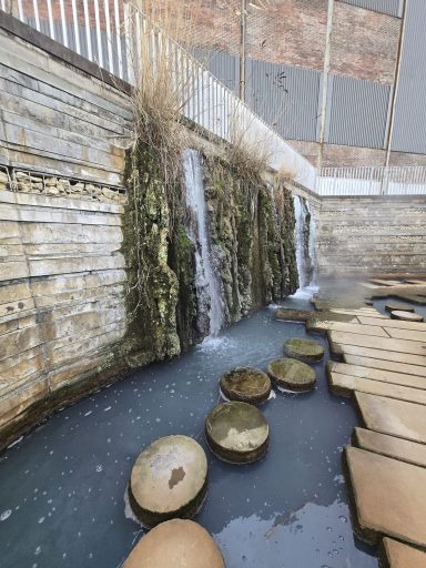 Kunstvolle Wasserspiele mit Steinen und Moos, umgeben von Holzplanken.
