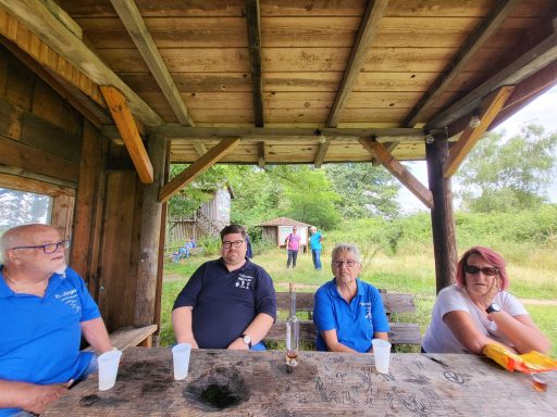 Gruppe von vier Personen in blauen Shirts, die an einem Tisch unter einer Überdachung sitzen.