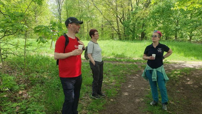 Drei Personen stehen auf einem Waldweg, umgeben von grüner Vegetation.