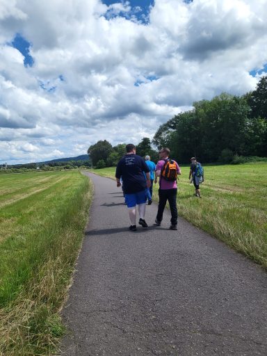 Gruppe von Menschen spaziert auf einem Weg durch eine grüne Landschaft unter bewölktem Himmel.