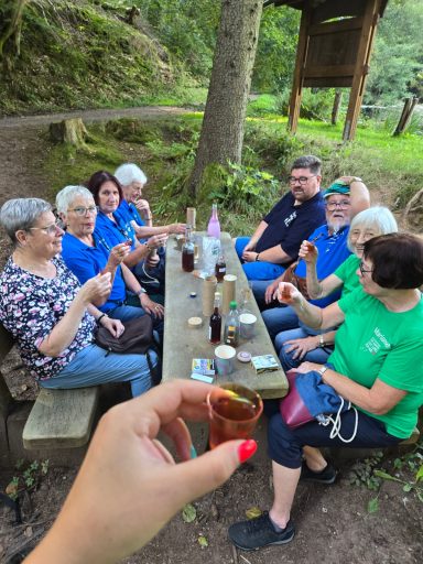 Gruppe von Menschen sitzt an einem Tisch im Freien, prostet mit Getränken.