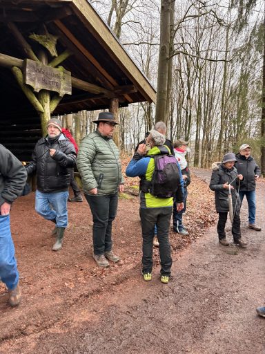 Gruppe von Wanderern in einem Wald, unter einem überdachten Bereich, im Gespräch.