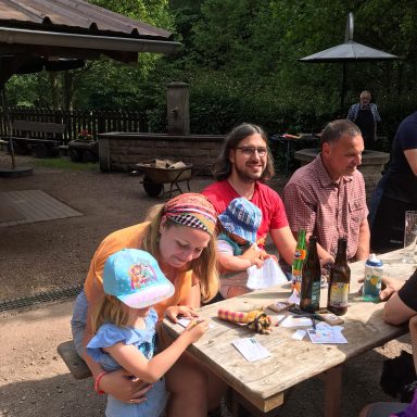 Eine Gruppe von Menschen sitzt an einem Tisch im Freien, umgeben von Bäumen.