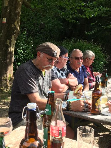 Gruppe von Menschen sitzt an einem Tisch im Freien, Getränke auf dem Tisch.