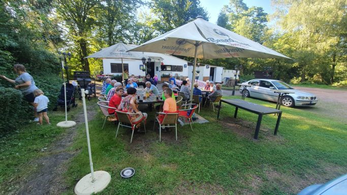 Eine Gruppe von Menschen sitzt an Tischen im Freien unter Sonnenschirmen.