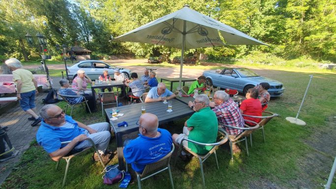 Gruppe von Menschen bei einem Treffen im Freien unter einem Sonnenschirm.