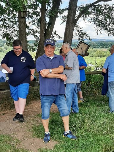 Männer stehen im Freien bei einem Treffen, mit Blick auf eine Landschaft im Hintergrund.
