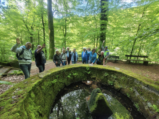 Gruppe von Menschen in einem Wald, umgeben von grünen Bäumen und einem kleinen Teich.
