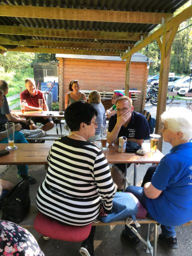 Menschen sitzen an Tischen im Freien und unterhalten sich in einer entspannten Atmosphäre.