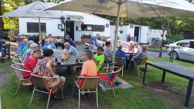 Gruppe von Menschen sitzt entspannt im Freien, um Tische in einem Gartenbereich.