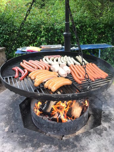 Eine Grillfläche mit verschiedenen Wurstsorten über einem offenen Feuer.