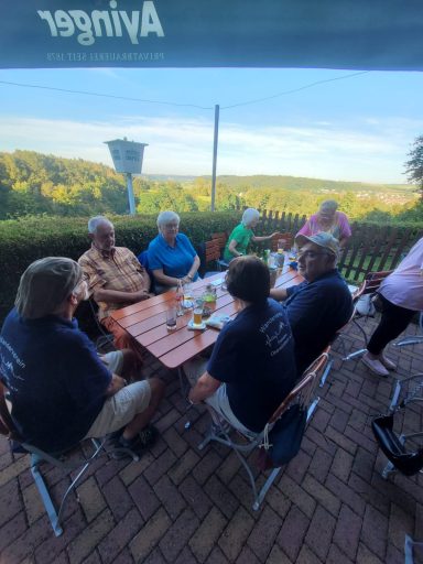 Gruppe von Personen, die entspannt an einem Tisch im Freien sitzen, mit Aussicht auf die Landschaft.
